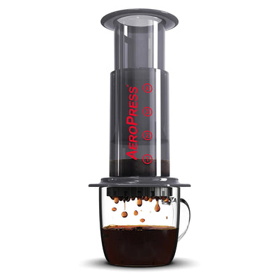 An AeroPress coffee maker with coffee dripping into the carafe, showing the coffee maker's clear body and black base.